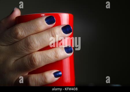 Photo d'une paire de mains avec ongles tenant une tasse à café rouge Banque D'Images