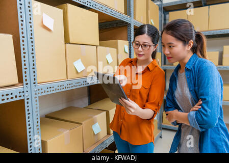 Belle jolie femme employés à l'aide de tampon mobile ordinateur travaillant en entrepôt et la navigation en ligne shopping commander le document pour confirmer de stock. Banque D'Images