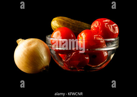 Poireau et de concombre salé avec des tomates en vase en verre. l'oignon et bol de tomates rouges et de concombre, isolé sur un fond noir Banque D'Images