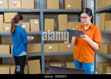 Jolie femme élégante tablette numérique mobile en utilisant le gestionnaire de groupe de travail et son employé girl contrôle de magasinage en ligne lorsqu'ils colis pour le comité permanent dans la guerre Banque D'Images