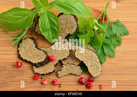 Tranches de truffe noire avec des plantes aromatiques, vert et rouge sur fond de bois Banque D'Images