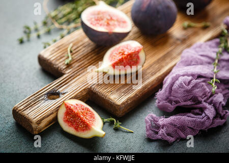Entier frais juteux et une coupe de fruits figues figs sur planche à découper en bois sur fond vert sombre Banque D'Images