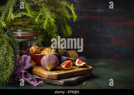 Entier frais juteux et une coupe de fruits figues figues et bol de miel en rayons sur la planche à découper en bois sur fond vert sombre Banque D'Images