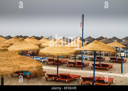 Des chaises vides et des parasols en chaume dans une plage solitaire dans un jour nuageux Banque D'Images