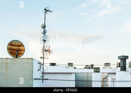 Les antennes de la télévision par satellite et d'antenne parabolique sur le toit blanc avec fond de ciel Banque D'Images