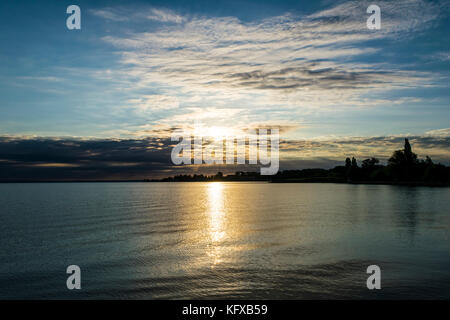 Beau lever de soleil sur le lac. Le soleil brille à travers les nuages de façon spectaculaire, silhouette d'arbres sur les rives du lac Balaton, en Hongrie. Banque D'Images