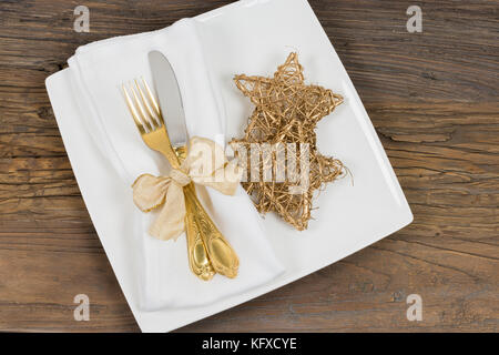 Noël dîner table cadre: Assiette carrée avec couverts d'or, serviette et étoiles de Noël dorées. Banque D'Images