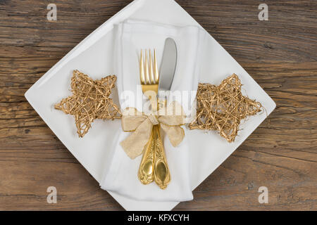 Noël dîner table cadre: Assiette carrée avec couverts d'or, serviette et étoiles de Noël dorées Banque D'Images