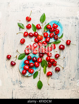 Cerises rouges savoureux avec des feuilles en bleu bols et table, vue de dessus la composition. fruits et baies concept Banque D'Images