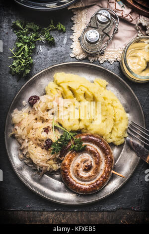 Saucisses grillées avec de la purée de pommes de terre et chou mariné dans la plaque de métal avec couverts servis sur table rustique foncé, vue du dessus, Close up. allemand traditi Banque D'Images