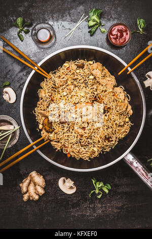 Nouilles frites épicées au wok casserole avec des baguettes sur fond sombre, rustique cuisine asiatique vue d'en haut. Banque D'Images