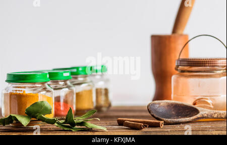 Épices et condiments conteneurs, pots en verre et bols dans une ligne, sur une surface en bois, avec mortier et pilon, bay leaf, cuillère en bois et un décor de cannelle Banque D'Images