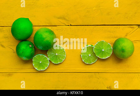 Citrons verts frais et colorés et de la chaux sur une surface de bois jaune, coupé en tranches et son ensemble, vue de dessus Banque D'Images