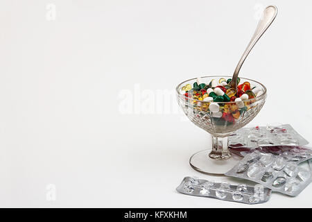 Comprimés de fond. Heap of assorted divers comprimés médecine et des pilules différentes couleurs dans bol en verre avec une cuillère à dessert et des boursouflures sur white backg Banque D'Images