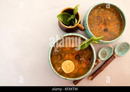 Soupe avec de la viande, viande fumée, saucisses, concombres, tomates, olives, herbes, citron dans un bol bleu sur fond de béton gris, des plats faits maison. Trad Banque D'Images