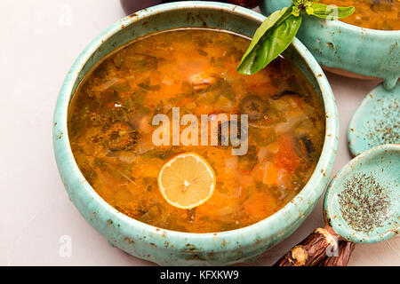 Soupe avec de la viande, viande fumée, saucisses, concombres, tomates, olives, herbes, citron dans un bol bleu sur fond de béton gris, des plats faits maison. Trad Banque D'Images