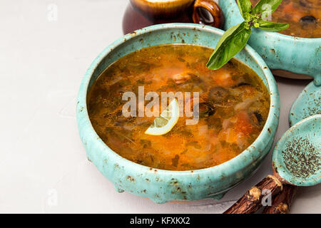 Soupe avec de la viande, viande fumée, saucisses, concombres, tomates, olives, herbes, citron dans un bol bleu sur fond de béton gris, des plats faits maison. Trad Banque D'Images