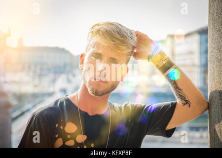 Blonde aux yeux bleus, beau jeune homme appuyé contre un mur en pierre et en plein air à la caméra à à Turin, Italie Banque D'Images