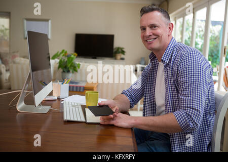 Portrait of smiling man holding mobile phone in living room Banque D'Images