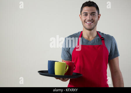 Portrait of smiling waiter holding un plateau avec les tasses de café Banque D'Images