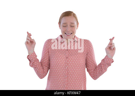 Smiling businesswoman holding ses doigts croisés contre fond blanc Banque D'Images