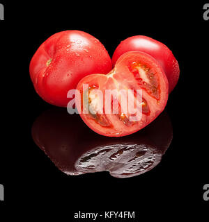Deux ensemble rouge et une demi-tomate couper libre isolé sur fond noir brillant avec du vrai réflexion. Vue de côté Banque D'Images