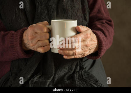 Old woman's hands holding froissé un mug avec un verre Banque D'Images