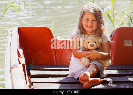 Portrait d'une douce petite fille assise dans le bateau et tenant son jouet préféré Banque D'Images