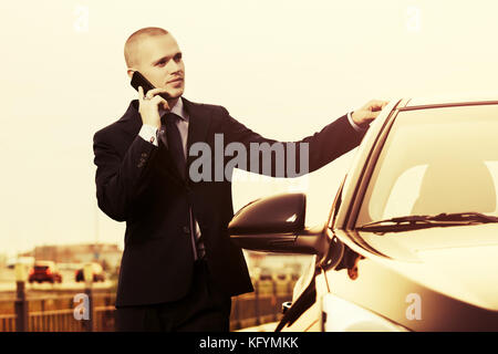 Young handsome businessman calling sur téléphone cellulaire près de sa voiture Banque D'Images