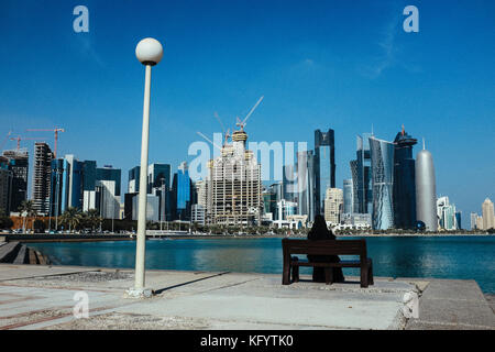 Doha, Qatar - 25 novembre 2013. Une femme musulmane est assis sur un banc et profiter de l'horizon de Doha. Banque D'Images