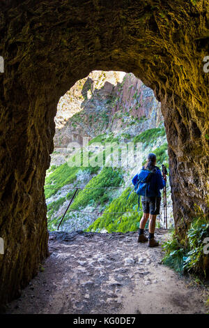 Female hiker traversant un tunnel sur la route de Pico do Arierio à Pico Ruivo - le plus haut sommet de Madère, Portugal Banque D'Images