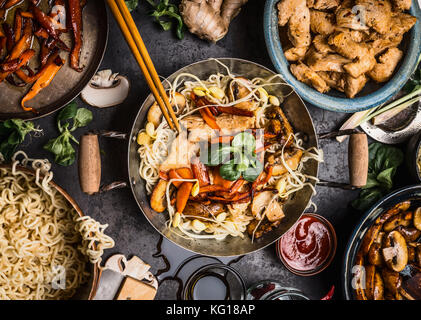 Table de cuisine asiatique avec des bols de nourriture, sauté au wok , baguettes , et les ingrédients sur l'arrière-plan, Vue de dessus Banque D'Images