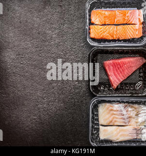 Divers de matières des filets de poissons : saumon, thon et morue dans les boîtes en plastique noir sur fond rustique, vue du dessus, frontière, place pour le texte. Fruits de mer sains c Banque D'Images