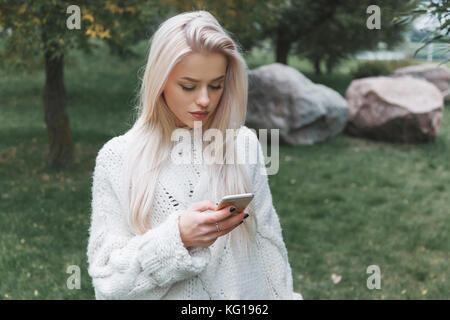 Cheveux blonds young caucasian woman in white pull utilise le téléphone piscine Banque D'Images