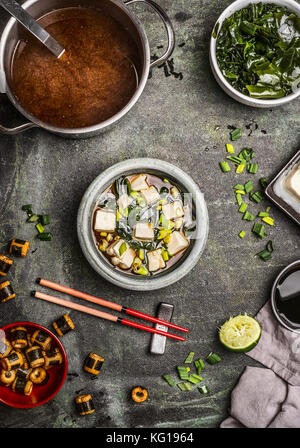 La soupe miso japonaise avec des ingrédients : algues wakame, tofu soyeux, et d'oignons de printemps, servi dans un bol sur la table avec des baguettes, vue du dessus Banque D'Images