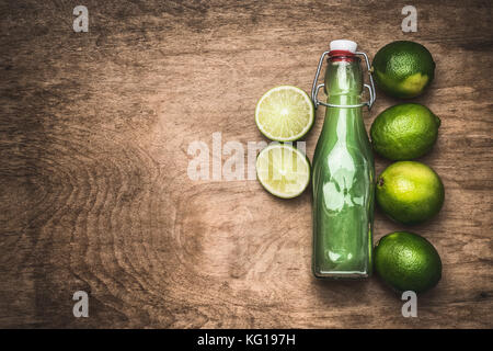 Jus de lime en bouteille avec fruits de citron vert sur fond de bois rustique, vue du dessus, la place pour le texte Banque D'Images