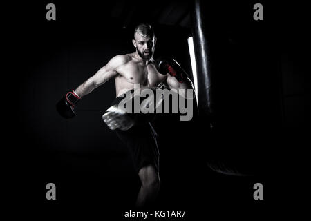 Boxer athlète masculin un sac de boxe boxe avec edgy spectaculaire dans un studio sombre lumineuse Banque D'Images