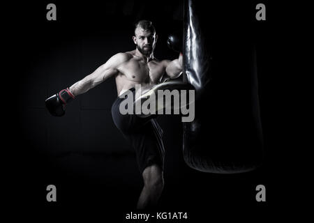 Boxer athlète masculin un sac de boxe boxe avec edgy spectaculaire dans un studio sombre lumineuse Banque D'Images