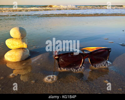 Lunettes de soleil et des chaussons chaussures sur la plage avec des pierres Banque D'Images