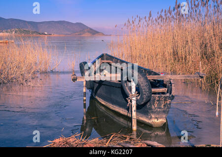 Bateau de pêche entouré de roseaux reflétée sur l'eau gelée du lac Prespa. Banque D'Images