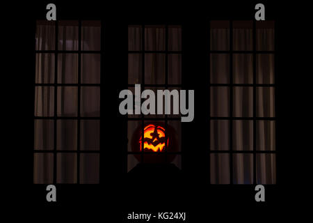 Citrouille Halloween, Jack o lantern face dans un cotswold cottage fenêtre. Cotswolds, Gloucestershire, Angleterre Banque D'Images