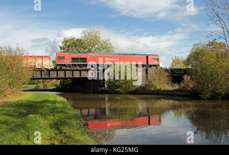 Une locomotive de fret rouge et son train sont reflétés dans les eaux du canal Trent et Mersey lorsqu'il la traverse près de Middlewich dans Cheshire. Banque D'Images