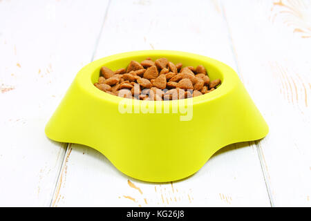 Bol vert-jaune avec des aliments secs pour chats sur un plancher en bois blanc Banque D'Images