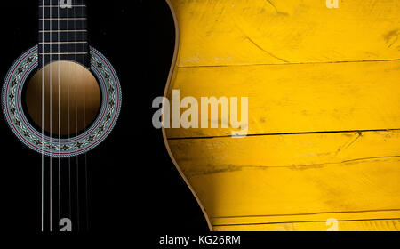 Corps de guitare acoustique noire libre, verticale, sur une table en bois jaune, l'arrière-plan avec beaucoup de texture, montrant la forme de guitare, cordes Banque D'Images