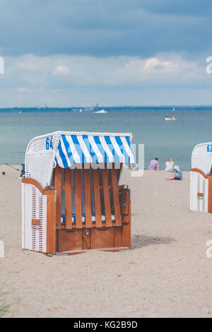 Colorfuled bar d'chaises couverte sur sable à Travemunde. Un couple sitting on beach en arrière-plan. Lübeck, Allemagne Banque D'Images