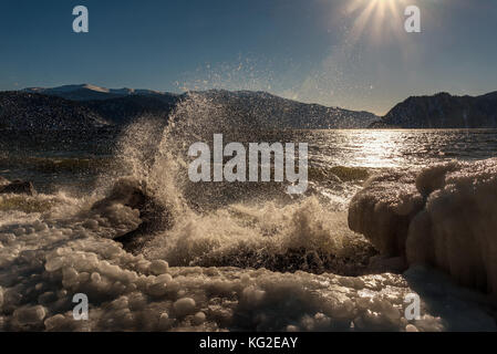 Une vue pittoresque de la mer, les montagnes, le soleil et la glace sur les roches à travers les paysages de la pulvérisation par le mouvement des vagues en hiver Banque D'Images