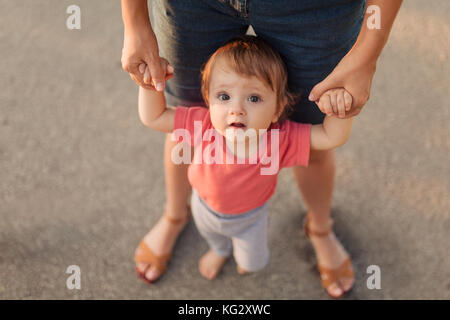 L'enseignement de mère fille bébé premiers pas à l'extérieur dans le coucher du soleil l'apprentissage de la marche Banque D'Images