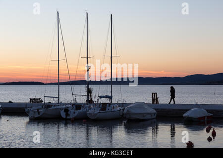 Un port sur un lac au coucher du soleil, avec des bateaux et une femme parlant au téléphone tout en marchant Banque D'Images