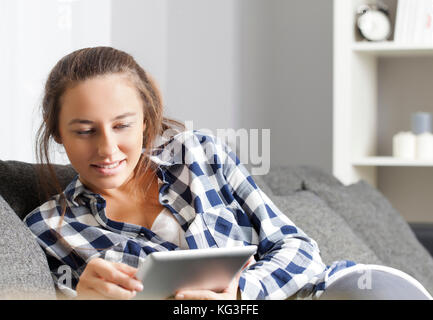 Femme lisant ebook sur ordinateur tablette tout en étant assis confortablement sur la table à la maison Banque D'Images