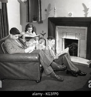 Années 1950, tableau historique des trois jeunes adultes dans une chambre à l'avant, deux assis sur un canapé en cuir, l'un assis sur le plancher, la lecture de livres, England, UK. Banque D'Images